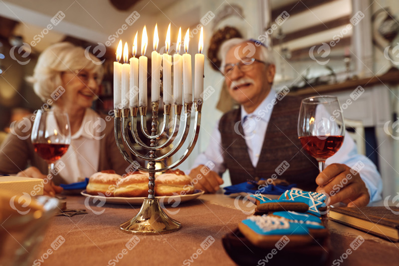 Close up of lit candles in menorah with happy senior Jewish coup