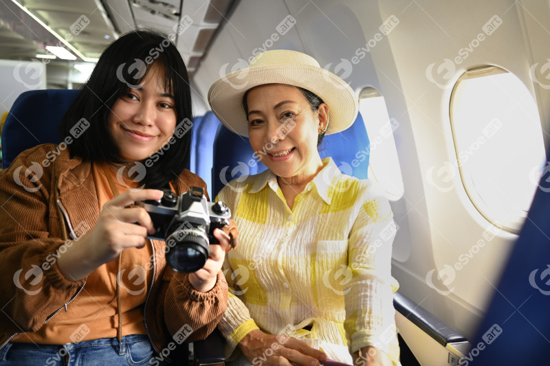 Happy senior woman and daughter sitting in passenger airplane and taking picture, waiting for airplane landing