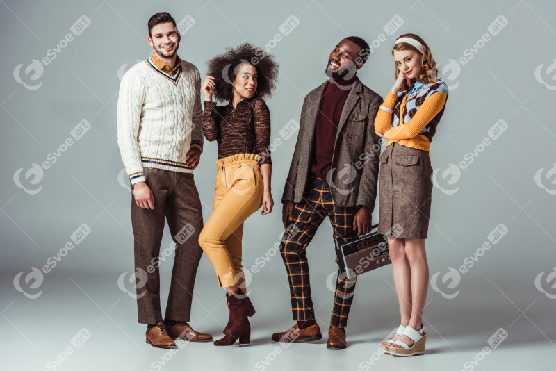 Smiling multicultural retro styled friends standing with vintage radio on grey