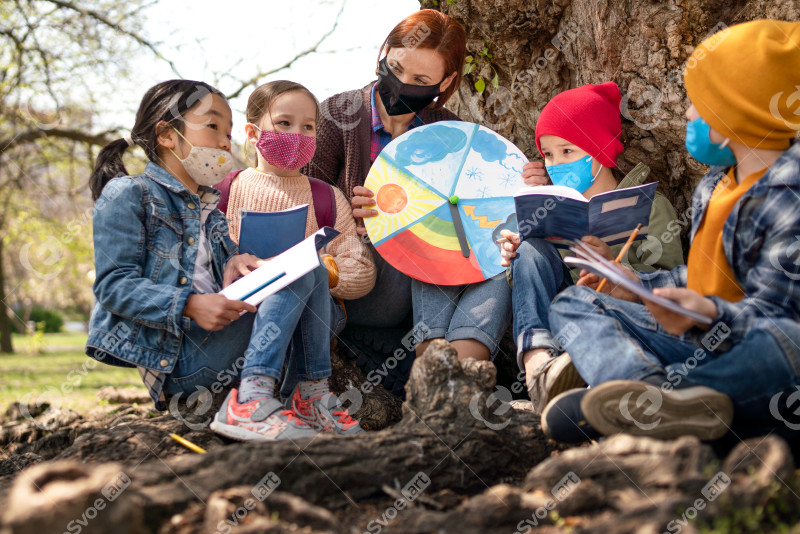 Teacher with small children sitting outdoors in city park, learning group education and coronavirus concept.